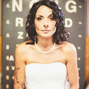 immagine demitizzante di una sposa con tatuaggio sul braccio davanti ad uno sfondo con il pannello oculistico